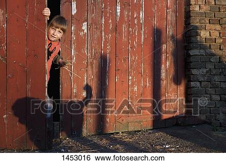 Stock Photograph - Portrait of girl peeking through barn door. Fotosearch