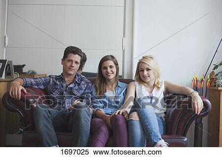 Stock Photography - Portrait of handsome man sitting beautiful female friends on sofa at home. Fotosearch