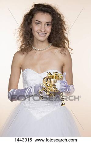 Stock Photography - Portrait of happy bride holding gift box against colored background. Fotosearch