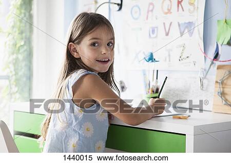 Stock Photography - Portrait of happy girl doing homework at desk. Fotosearch