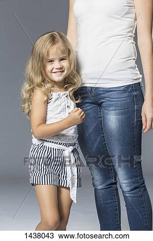 Stock Image - Portrait of happy girl standing with mother against gray background. Fotosearch