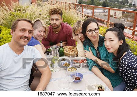 Stock Photo - Portrait of happy male and female friends sitting at outdoor table at patio. Fotosearch
