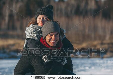 Portrait of happy man giving piggyback ride to woman during winter View Large Photo Image Stock Photography - Portrait of happy man giving piggyback ride to woman during winter. Fotosearch