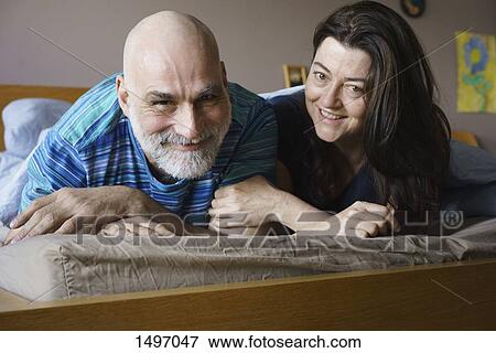 Stock Photo - Portrait of happy mature couple lying on bed at home. Fotosearch