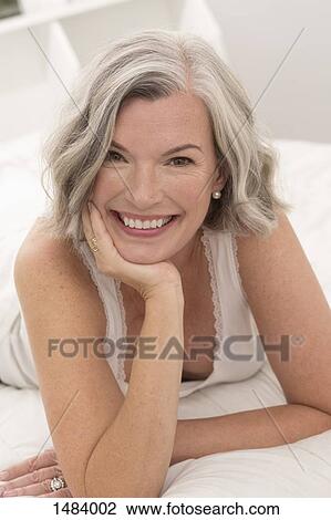 Stock Image - Portrait of happy mature woman lying on bed at home. Fotosearch