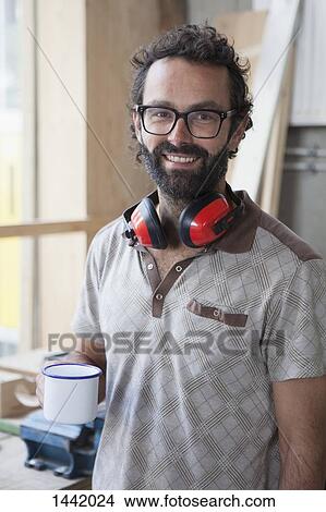 Picture - Portrait of happy mid adult carpenter having coffee in workshop. Fotosearch