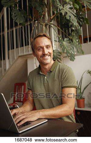 Portrait of happy mid adult man using laptop at table View Large Photo Image Stock Photo - Portrait of happy mid adult man using laptop at table. Fotosearch