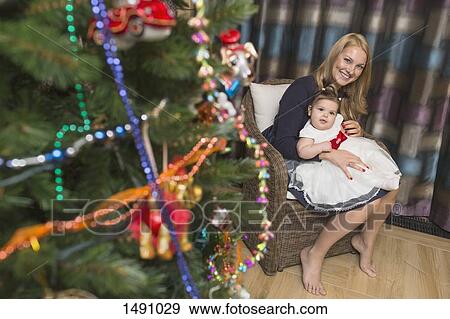 Portrait of happy mother sitting with baby girl celebrating Christmas View Large Photo Image Stock Photo - Portrait of happy mother sitting with baby girl celebrating Christmas. Fotosearch