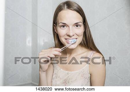 Stock Image - Portrait of happy woman brushing teeth in domestic bathroom. Fotosearch