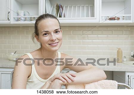 Stock Photo - Portrait of happy woman sitting in domestic kitchen. Fotosearch