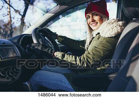 Picture - Portrait of happy young woman in warm clothing driving car. Fotosearch