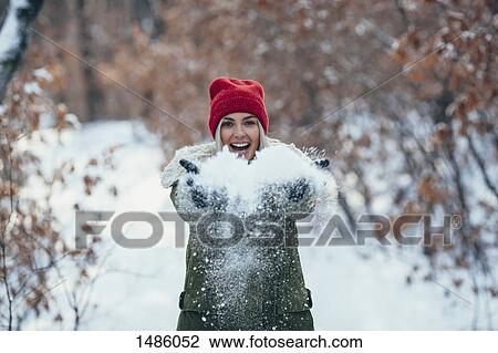 Stock Image - Portrait of happy young woman playing with snow. Fotosearch
