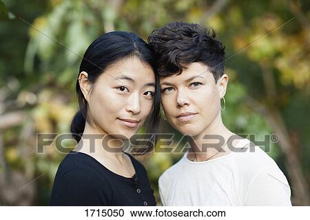 Stock Image - Portrait of lesbian couple standing at park. Fotosearch