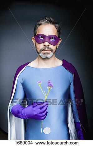 Portrait of man dressed as superhero holding flower against gray background View Large Photo Image Picture - Portrait of man dressed as superhero holding flower against gray background. Fotosearch