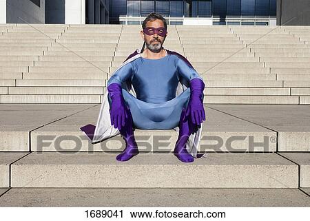 Stock Image - Portrait of man dressed as superhero sitting on steps. Fotosearch