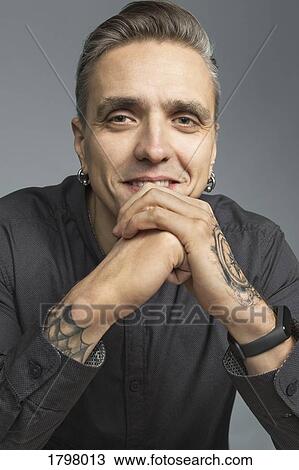 Portrait of man smiling and resting chin on hands against gray background View Large Photo Image Stock Image - Portrait of man smiling and resting chin on hands against gray background. Fotosearch