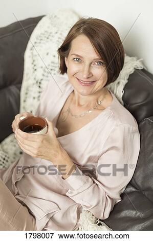 Portrait of mature woman smiling while sitting with hot drink View Large Photo Image Stock Photo - Portrait of mature woman smiling while sitting with hot drink. Fotosearch