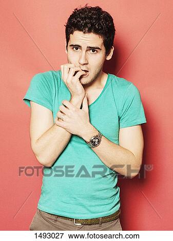 Stock Photo - Portrait of nervous young man biting nails against red background. Fotosearch