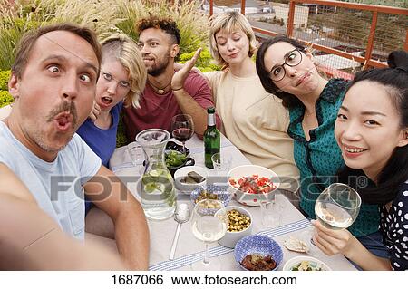 Portrait of playful friends making faces while sitting at outdoor table at patio View Large Photo Image Stock Photograph - Portrait of playful friends making faces while sitting at outdoor table at patio. Fotosearch
