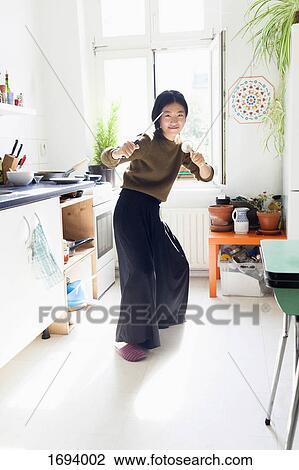 Stock Image - Portrait of playful woman gesturing with knife and strainer in kitchen. Fotosearch