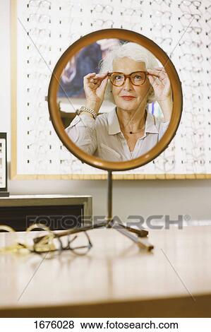 Portrait of senior woman wearing eyeglasses reflecting on mirror at store View Large Photo Image Stock Photo - Portrait of senior woman wearing eyeglasses reflecting on mirror at store. Fotosearch
