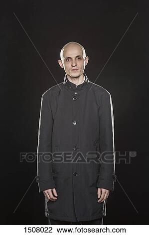 Stock Image - Portrait of serious bald man standing against black background. Fotosearch