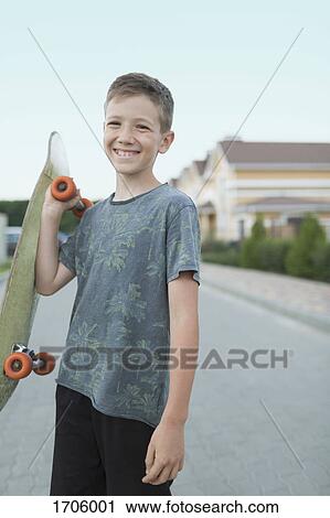 Portrait of smiling boy holding skateboard while standing on street View Large Photo Image Stock Image - Portrait of smiling boy holding skateboard while standing on street. Fotosearch