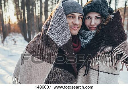 Stock Photo - Portrait of smiling couple wrapped in blanket while standing on snow covered field. Fotosearch