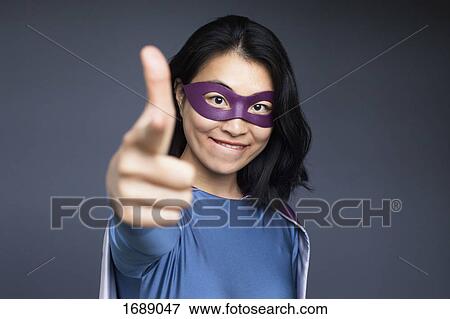 Stock Photo - Portrait of smiling female superhero pointing against gray background. Fotosearch