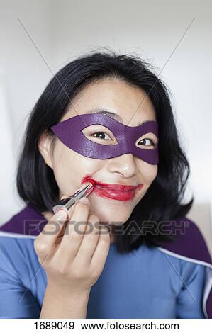 Stock Photo - Portrait of smiling female superhero wearing red lipstick against gray background. Fotosearch