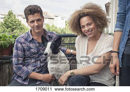 Portrait of smiling friends with dog sitting by man in balcony View Large Photo Image Stock Image - Portrait of smiling friends with dog sitting by man in balcony. Fotosearch