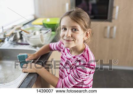 Stock Photo - Portrait of smiling girl holding cleaning sponge at kitchen sink. Fotosearch