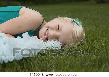 Stock Photo - Portrait of smiling girl lying on grassy field at backyard. Fotosearch