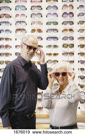 Portrait of smiling man and woman wearing sunglasses while standing at store View Large Photo Image Stock Photo - Portrait of smiling man and woman wearing sunglasses while standing at store. Fotosearch