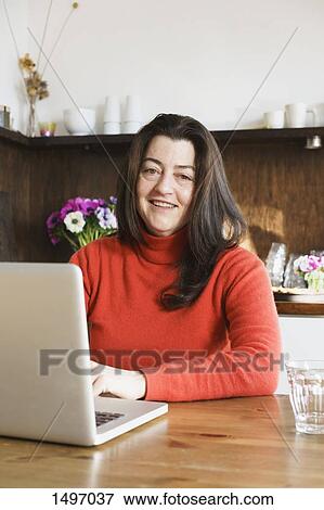 Portrait of smiling mature woman using laptop at home View Large Photo Image Stock Photo - Portrait of smiling mature woman using laptop at home. Fotosearch