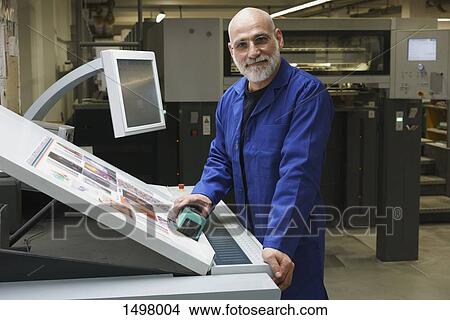 Picture - Portrait of smiling mature worker standing by equipment at printing press. Fotosearch