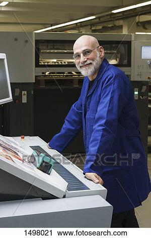 Stock Image - Portrait of smiling mature worker standing by equipment at printing press. Fotosearch