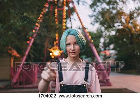 Stock Image - Portrait of smiling teenage girl holding illuminated sparkler. Fotosearch
