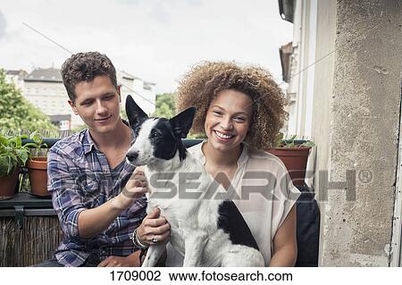 Portrait of smiling woman carrying dog sitting with friend in balcony View Large Photo Image Stock Image - Portrait of smiling woman carrying dog sitting with friend in balcony. Fotosearch