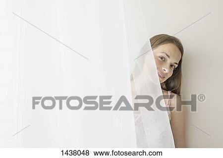 Stock Photo - Portrait of smiling woman hiding behind curtain at home. Fotosearch