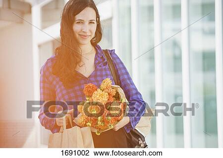 Portrait of smiling woman holding flower bouquet standing against building View Large Photo Image Stock Image - Portrait of smiling woman holding flower bouquet standing against building. Fotosearch