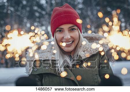 Stock Photo - Portrait of smiling woman holding sparklers during winter. Fotosearch