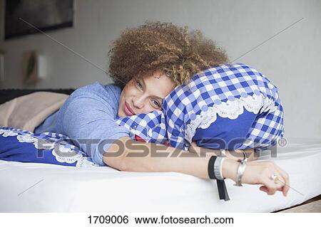Portrait of smiling woman holding pillow while lying on bed at home View Large Photo Image Stock Photograph - Portrait of smiling woman holding pillow while lying on bed at home. Fotosearch
