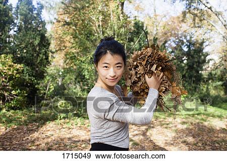 Stock Photo - Portrait of smiling woman throwing dry leaves while standing at park. Fotosearch