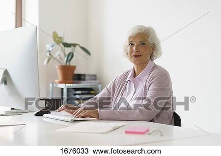 Portrait of smiling woman using computer while sitting against wall in office View Large Photo Image Stock Image - Portrait of smiling woman using computer while sitting against wall in office. Fotosearch