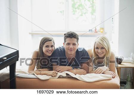 Stock Photo - Portrait of smiling young friends lying on bed at home. Fotosearch