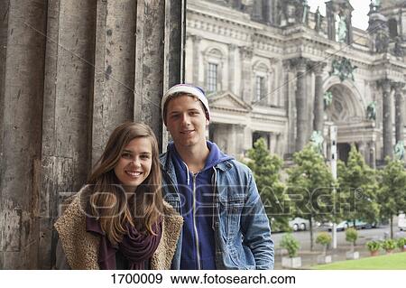 Stock Photo - Portrait of smiling young friends standing by column at Altes Museum against Berlin Cathedral. Fotosearch