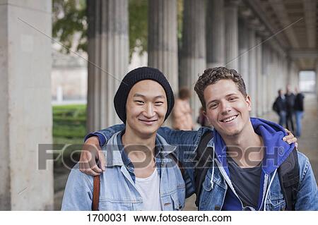 Portrait of smiling young male friends standing with arms around, Berlin, Germany View Large Photo Image Stock Image - Portrait of smiling young male friends standing with arms around, Berlin, Germany. Fotosearch