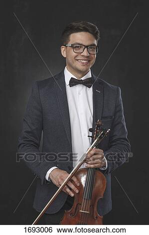 Portrait of smiling young man holding violin while standing against black background View Large Photo Image Stock Photograph - Portrait of smiling young man holding violin while standing against black background. Fotosearch