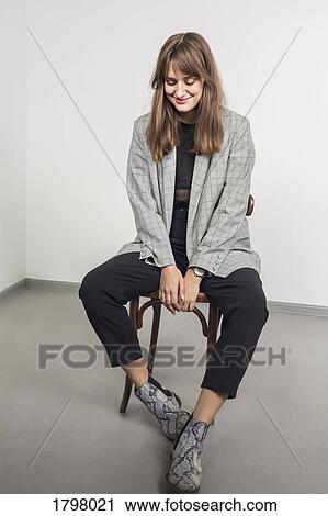 Stock Image - Portrait of stylish woman with long brown hair sitting on chair. Fotosearch